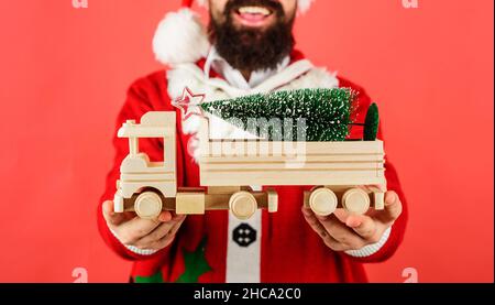 Santa con albero di Natale su camion giocattolo in legno. Consegna, natale, Capodanno. Messa a fuoco selettiva. Foto Stock