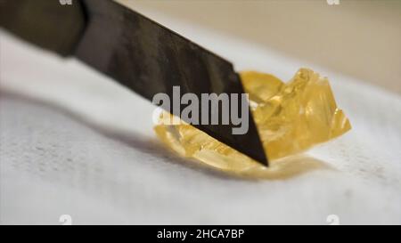 Primo piano estremo per pietra minerale giallo trasparente toccata da taglierina su sfondo bianco tessuto. Golden, piccolo pezzo di pietra minerale che giace sul Foto Stock