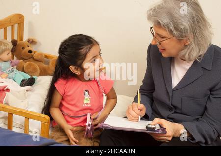 Ricercatore sulla visita domestica alla ragazza di tre anni che interagisce con lei e prendendo note la famiglia è ricercatore messicano americano è bianco Foto Stock