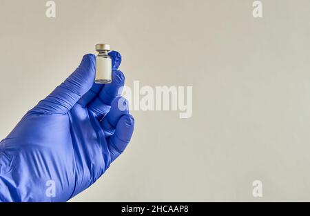Mano con un guanto blu, che contiene un piccolo flaconcino contenente un vaccino, che sta per essere usato. Foto Stock