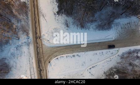 Incrocio a T nella foresta innevata durante la giornata invernale. Vista aerea. Riprese. Auto a bordo di un bivio nella foresta innevata nei giorni invernali. Vista aerea Foto Stock