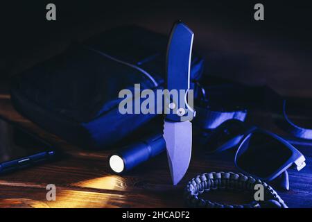 Set tattico per il trasporto quotidiano o la sopravvivenza EDC per l'uomo moderno in luce blu. Coltello automatico tascabile, torcia, parabordo e borsa. Foto Stock