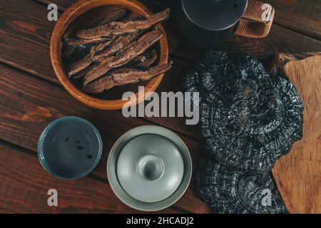 Lingzhi cinese essiccato in ciotola e pezzi tagliati a fette di Ganoderma Lucidum o Reishi fungo in piatto su tavola di legno vista dall'alto. Erbe asiatiche per la salute. Medicina di erbe. Foto Stock