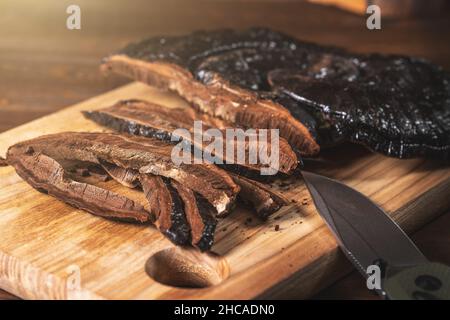 Affettato su pezzi Ling Zhi erbe naturali cinesi o Reishi funghi, Ganoderma su cucina scrivania in legno. Medicina organica a base di erbe. Foto Stock