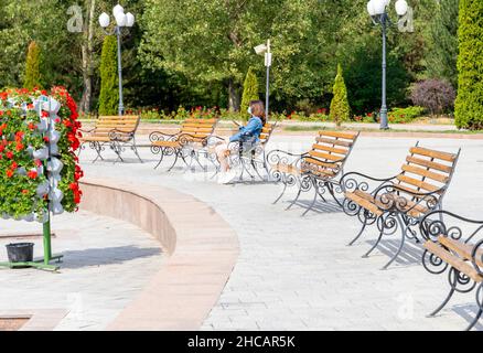 Donna seduta sulla panchina nel primo Parco del Presidente - un punto di riferimento urbano ad Almaty, Kazakhstan Foto Stock