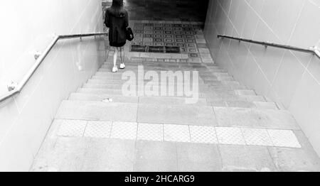 Una donna, vista da dietro camminando giù le scale per entrare nel passaggio. Concetto: Da solo, camminando giù, pericolo, libro o copertina album Foto Stock