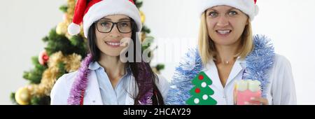 Dentisti femminili che indossano cappelli di babbo natale che tengono mascella e albero di natale Foto Stock
