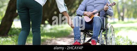 L'uomo in sedia a rotelle suona la chitarra nei passanti del parco-da dare soldi. Foto Stock