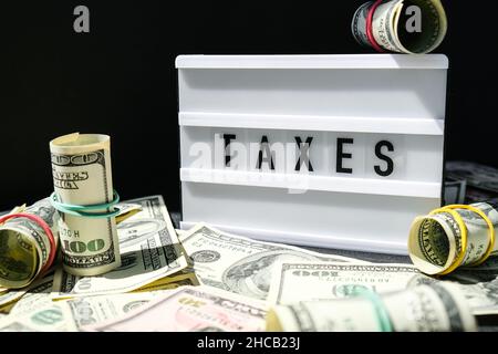 Cartoncino con le tasse in lettere nere intorno a noi banconote in dollari. Pagamento delle imposte e concetto di deposito. Denaro, Business, finanza, investimenti Foto Stock