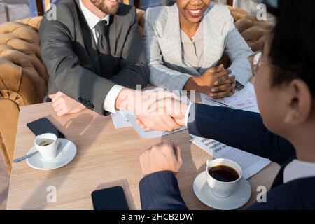 Handshake di due partner aziendali di successo sopra il tavolo con carte e tazze di caffè dopo la firma del nuovo contratto Foto Stock