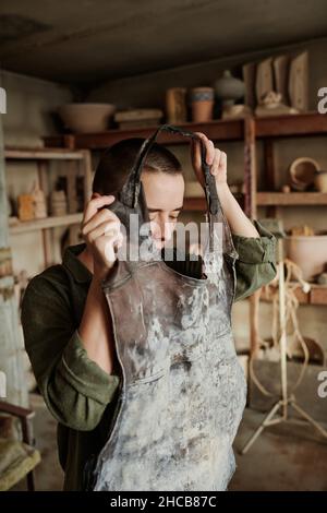 Giovane donna che indossa il grembiule da lavoro, si prepara al lavoro in officina Foto Stock