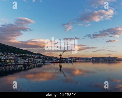 Dawn al lungofiume di Bergens guardando verso il vecchio porto di pesca con le sue gru onshore e le nuvole che si riflettono nelle acque della camma Foto Stock