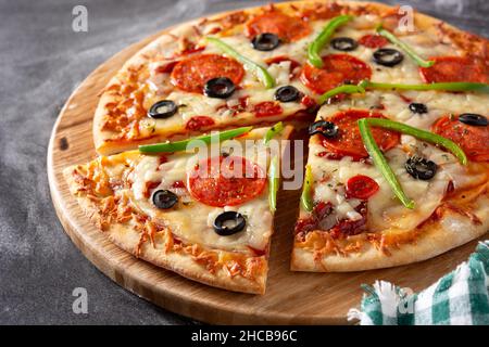 Pizza tradizionale suprema su un rustico tavolo di legno Foto Stock