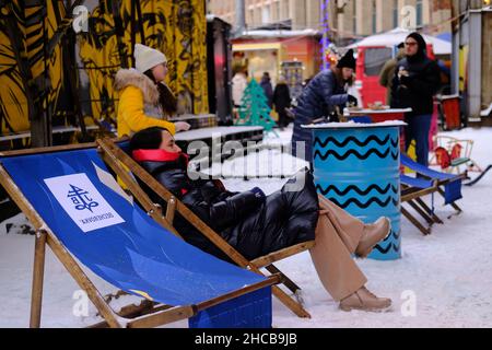 Minsk, Bielorussia, 25 dicembre 2021: Una donna siede su una sedia a sdraio alla fiera di Capodanno. La gente cammina e si diverte. Foto Stock