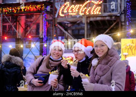 Minsk, Bielorussia, 25 dicembre 2021: Tre donne, fidanzate alla fiera di Capodanno, mangiare cibo di strada e divertirsi. Foto Stock