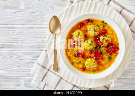 Anar di Ash-e, zuppa invernale di melagrana gialla in due pezzi con polpette, zuppa spessa, in una ciotola bianca su un tavolo di legno bianco testurizzato, piatto, f Foto Stock