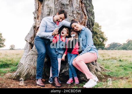 Famiglia felice godendo lollipops vicino albero nel parco Foto Stock