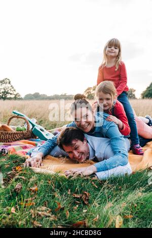 Genitori giocosi con figlie sdraiate su coperta nel parco Foto Stock