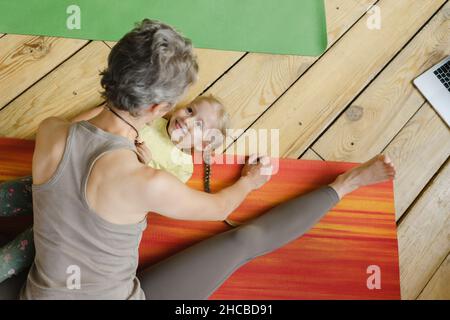 Ragazza sorridente che guarda la madre che si esercita sul pavimento Foto Stock