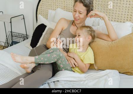 Felice figlia che riposa con la madre a letto a casa Foto Stock