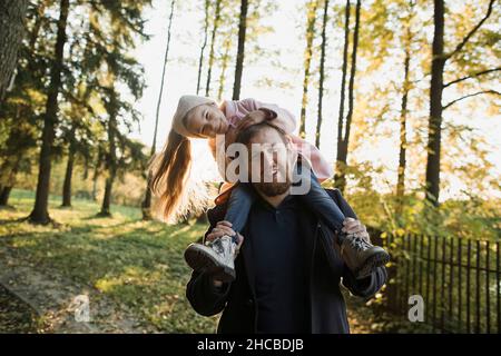 Padre che porta una figlia giocosa sulle spalle al tramonto Foto Stock
