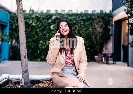 Donna d'affari sorridente che parla sul telefono cellulare per albero Foto Stock
