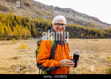 Sorridente escursionista senior che detiene contenitore di bevande isolato a Rhaetian Alps, Italia Foto Stock