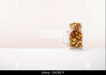 Vaso di vetro riempito con una varietà di noci con uno sfondo bianco o bitonale. Foto Stock