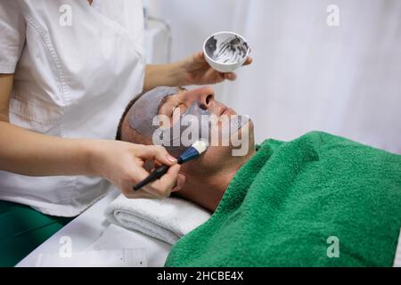 Beautician applicare maschera facciale con spazzola sul viso del cliente in salone di bellezza Foto Stock