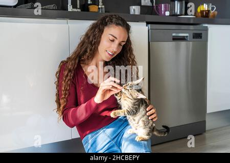 Giovane donna che alimenta il gatto in cucina Foto Stock