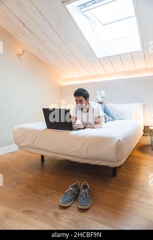 Un freelance sorridente che si trova a letto utilizzando un computer portatile Foto Stock