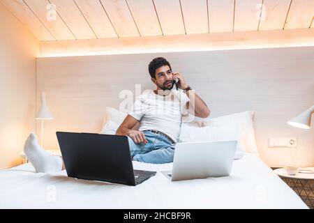 Uomo d'affari che parla di smart phone tenendo un documento sul letto a casa Foto Stock