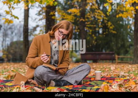 Donna con libro lettura penna in autunno parco Foto Stock