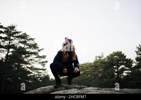 Donna accovacciata su roccia nella foresta Foto Stock