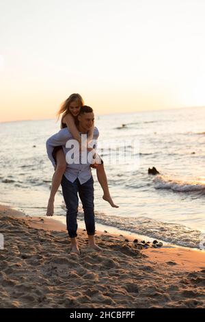 Donna giocosa piggybacking su uomo in spiaggia Foto Stock