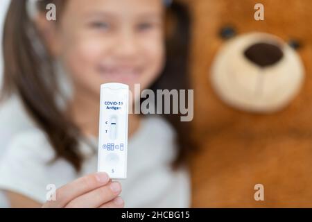 Ragazza sorridente con orsacchiotto che mostra un rapido risultato diagnostico del test Foto Stock