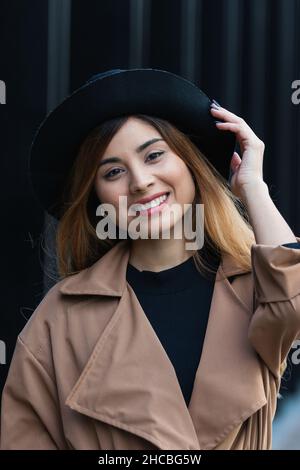 Donna che tiene il cappello di fronte al muro nero Foto Stock