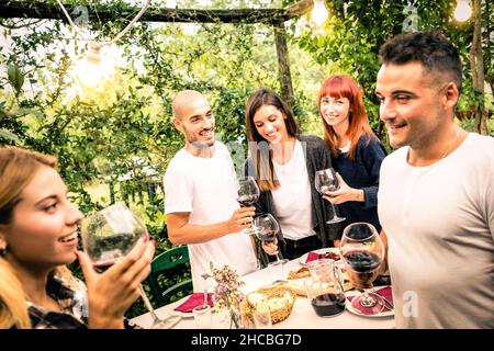 Amici felici divertirsi bevendo vino rosso a festa giardino cortile - concetto di gioventù e amicizia insieme alla cantina fattoria vigneto Foto Stock