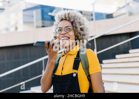 Donna sorridente che invia messaggi vocali tramite telefono cellulare in pochi passaggi Foto Stock