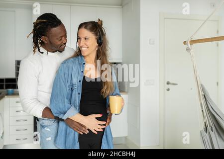 Uomo che abbraccia una donna incinta sorridente a casa Foto Stock