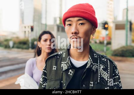Giovane uomo con cappello a maglia rossa con donna sullo sfondo Foto Stock