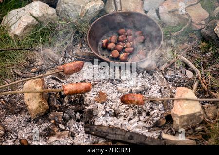 Salsicce e castagne cucinate al fuoco nel bosco Foto Stock