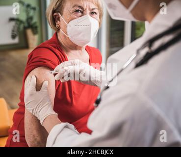 Donna anziana con maschera facciale che viene vaccinata a casa Foto Stock