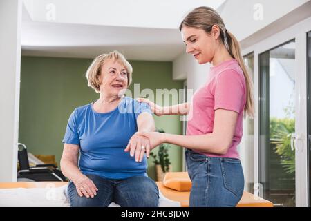 Giovane fisioterapista che aiuta il paziente a tendere la mano a casa Foto Stock