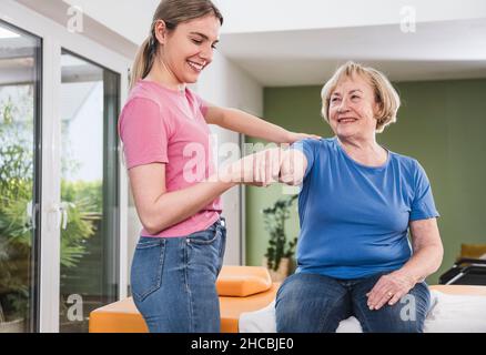 Fisioterapista che allunga la mano della donna disabile a casa Foto Stock