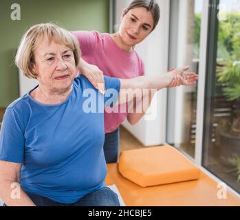 Fisioterapista massaggiante la spalla del paziente disabile Foto Stock