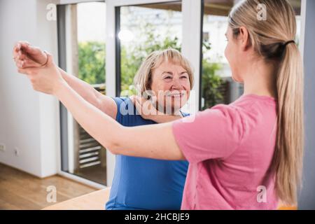 Donna sorridente che si esercita con il sostegno del fisioterapista a casa Foto Stock