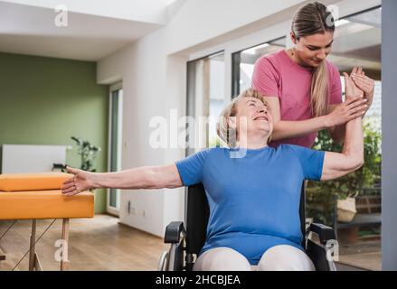 Fisioterapista massaggiando la mano della donna disabile in sedia a rotelle a casa Foto Stock