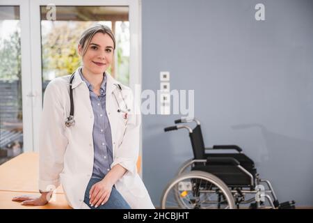 Giovane medico che indossa un camice da laboratorio seduto a casa Foto Stock