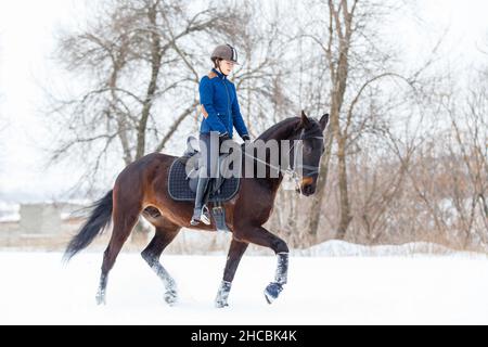 Giovane donna a cavallo nel parco invernale sulla neve Foto Stock